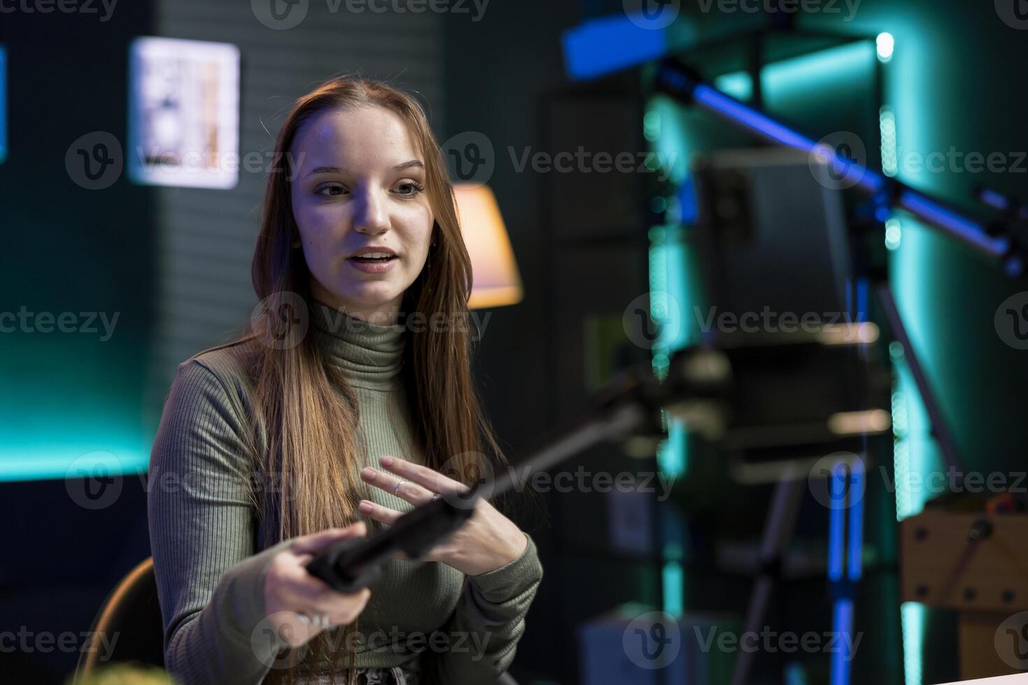 Young girl using smartphone attached to selfie stick to film content for her online fans, talking about gen Z topics. Happy person recording vlog for internet channel with cellphone camera photo