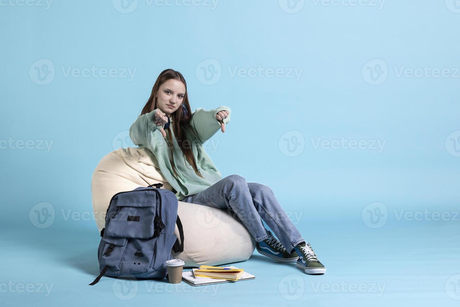 Portrait of upset schoolgirl showing thumbs down sign, disappointed about university exams, studio background. Young girl does disapproving negative hand gesturing regarding homework photo