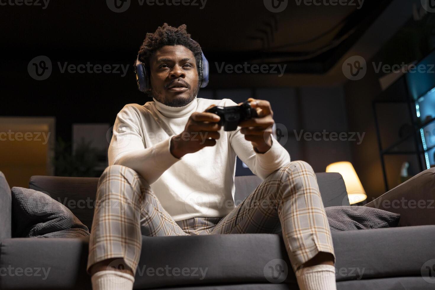 Man focused on defeating enemies while playing videogames on gaming console with teammates, talking through headphones. Gamer fights rival players using gamepad, chatting with friends through headset photo