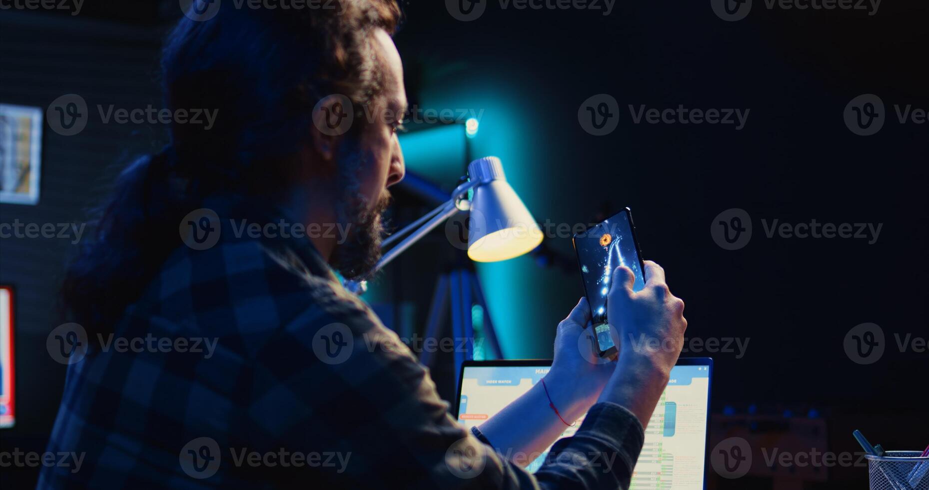 Man playing videogames on cellphone, relaxing in living room after analyzing financial graphs all day. Gamer enjoying science fiction shooter game on mobile phone, having fun, camera B photo