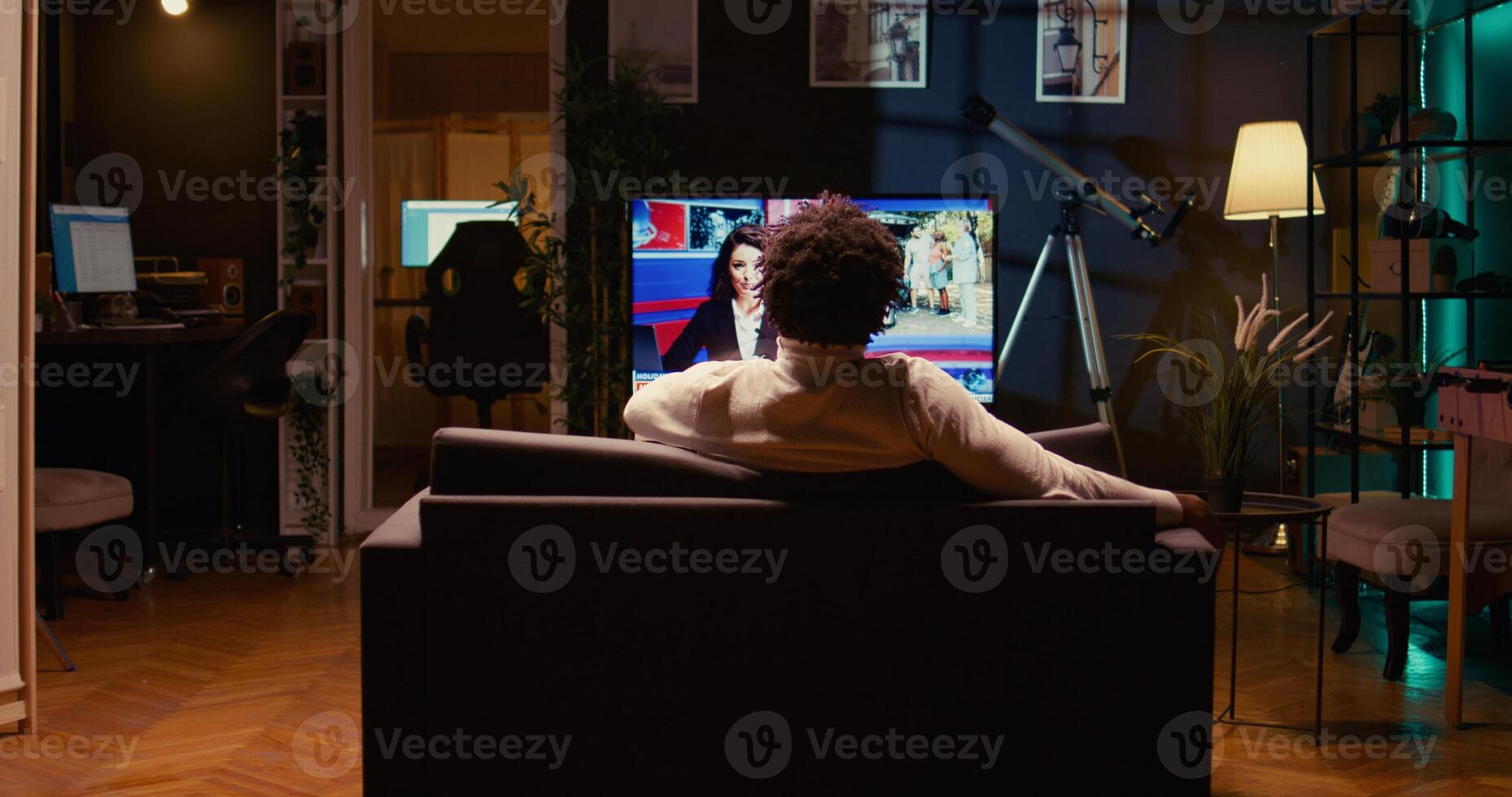 Man holding remote, looking at latest news on TV after zapping through channels. Zoom in shot on person using ultrawide smart TV in neon lit living room to entertain himself after work photo