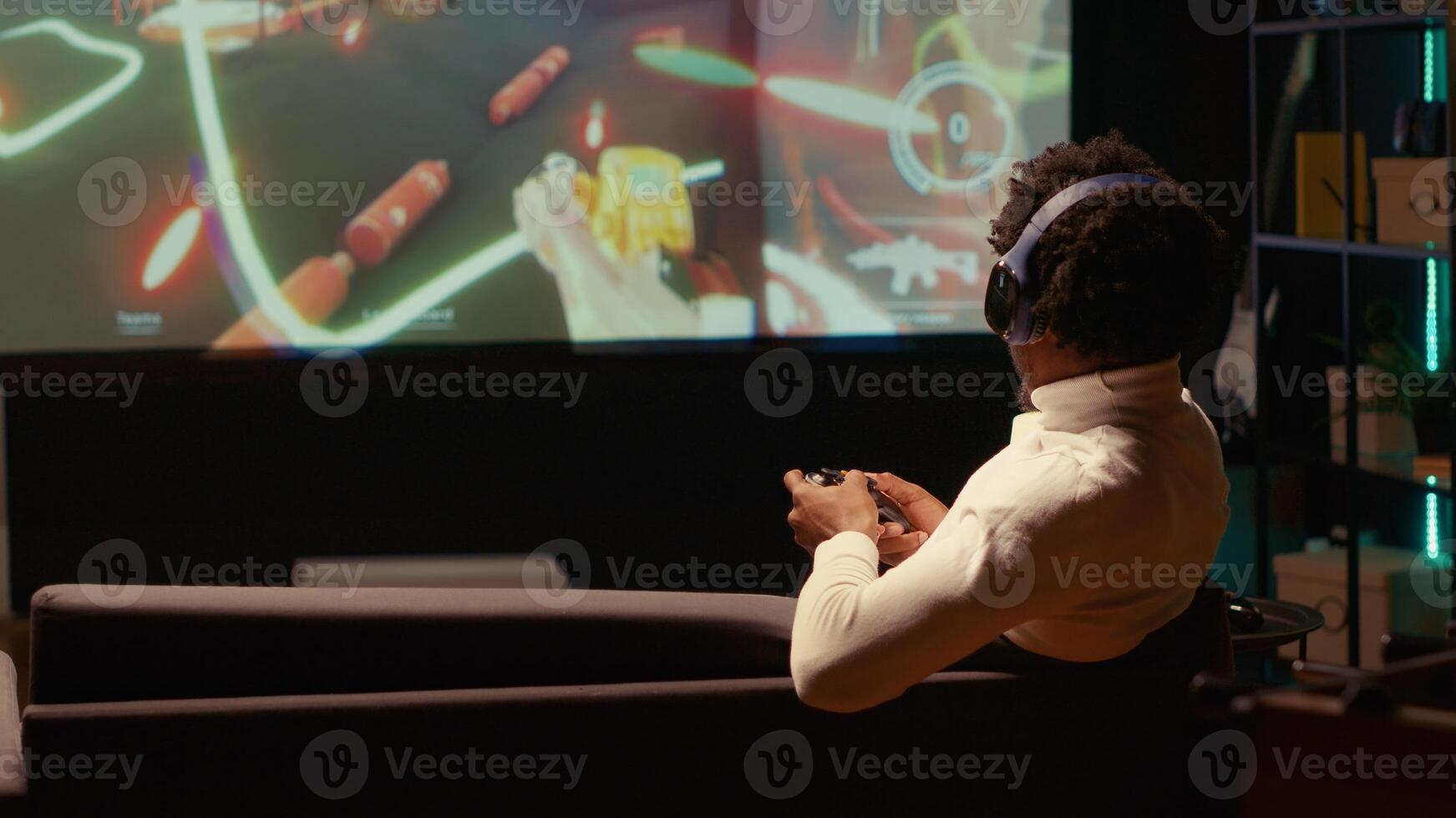 Man playing singleplayer videogames on ultrawide smart TV, putting headphones on to feel immersed. BIPOC gamer using controller to beat science fiction shooter game on gaming console photo