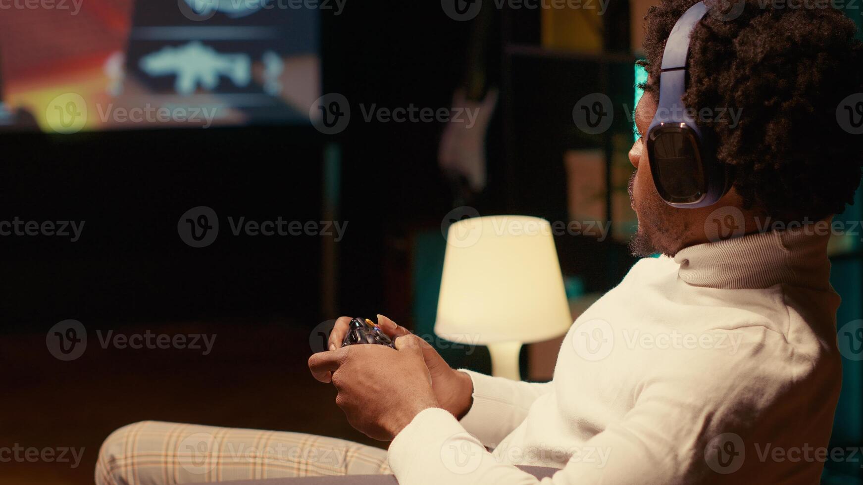 Gamer playing first person shooter game on ultrawide smart TV, communicating with teammates using headphones. African american man reaching final mission in FPS videogame photo
