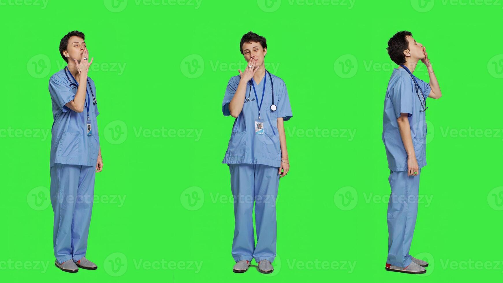 Flirty cute nurse blowing air kisses against greenscreen backdrop, being romantic and expressing sweet feelings. Medical assistant in scrubs doing lovely gesture, expressing true love. Camera A. photo