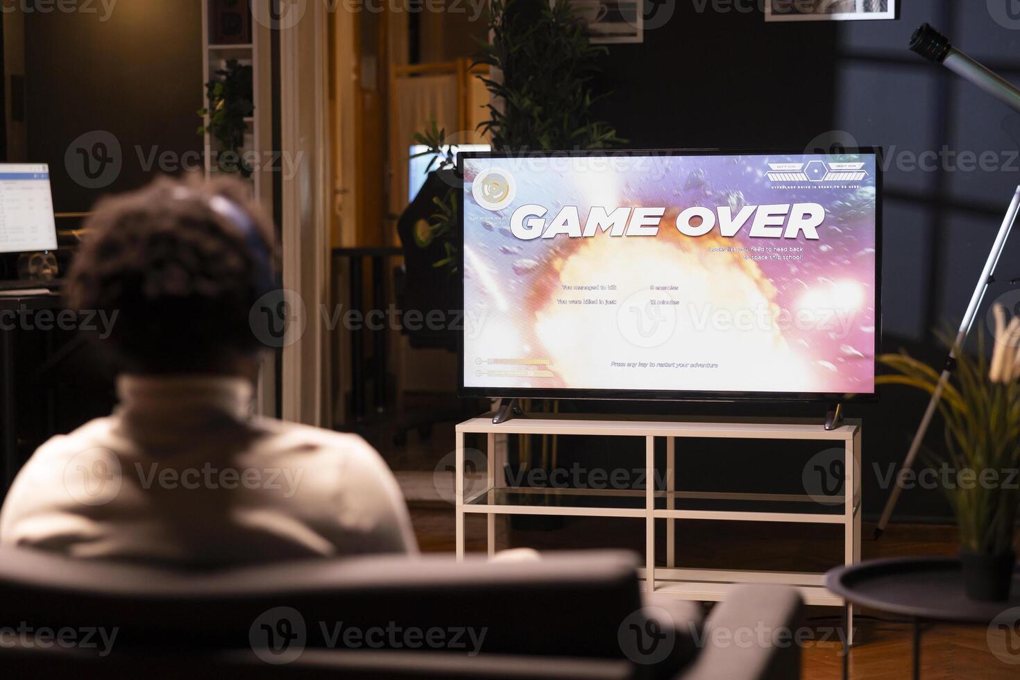 Man looking at game over screen of science fiction videogame on smart TV. African american gamer receiving defeat message after failing to beat level, watching statistics roll on display photo