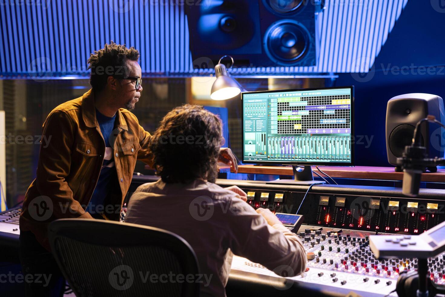 Post production team working on editing sound settings in studio, audio software interface on computer. Artist and sound technician applying mixing and mastering techniques to create a hit. photo