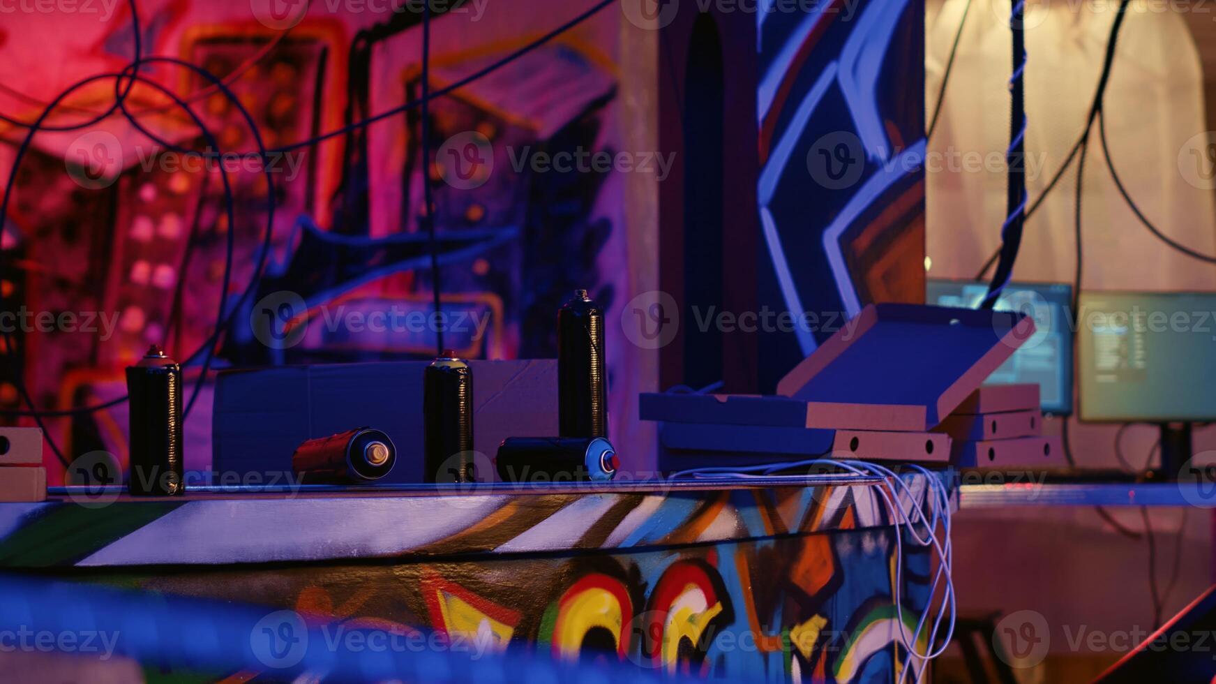Panning shot of empty spray cans and pizza boxes in messy abandoned warehouse with graffiti sprayed on walls. Rundown urban hideout with Hacking software running on background computers photo