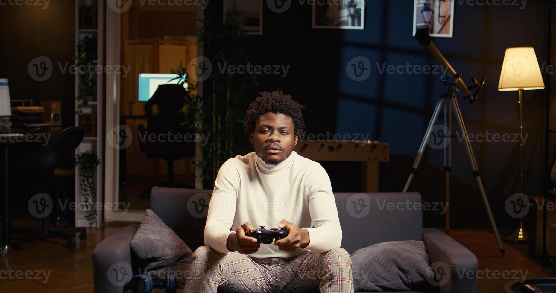 Man focused on playing singleplayer videogames on TV in cozy living room. BIPOC gamer using controller to beat science fiction shooter game on gaming console, relaxing on couch photo