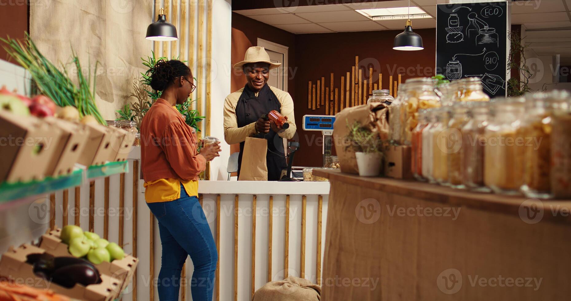 African american seller preparing bag with products for client, weighting fruits and veggies. Merchant scanning bulk items in recyclable jars, woman supporting nonpolluting business. Camera 2. photo