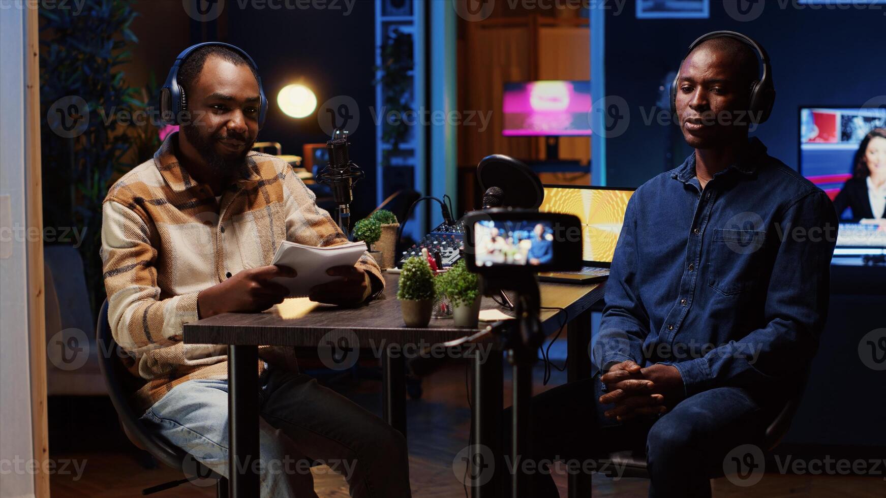 Content creator recording interview with professional camera in studio, reviewing notes to ask pertinent questions to guest. Journalist using filming gear, talking on mic with african american man photo