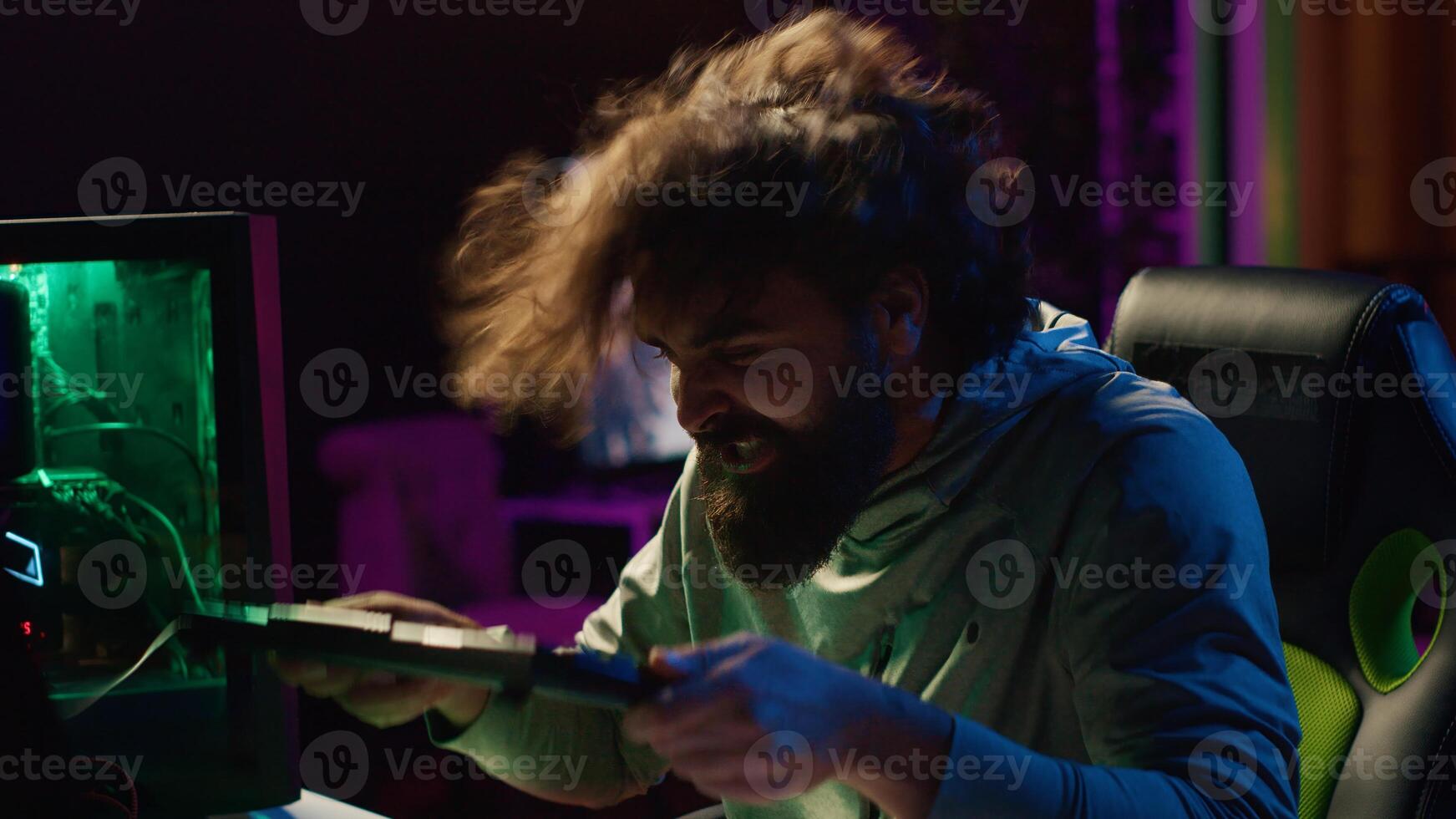 Furious gamer smashing keyboard on head after losing online competitive multiplayer match. Close up shot of livid man feeling exasperated after being defeated in videogames photo