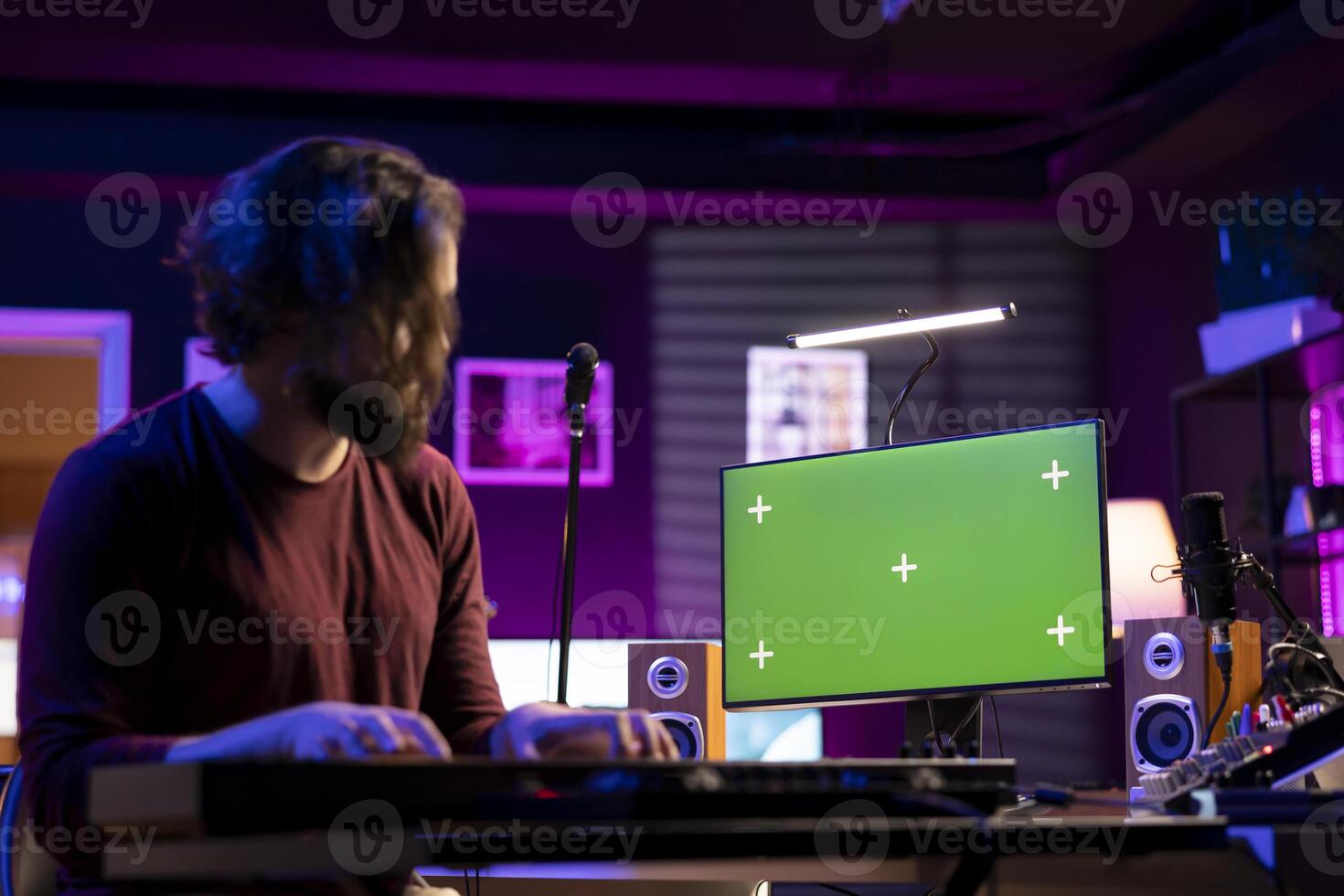 Music producer composing a melody on midi controller keyboard and watching online lessons on computer with greenscreen. Songwriter playing electronic piano in home studio, producing tunes. photo