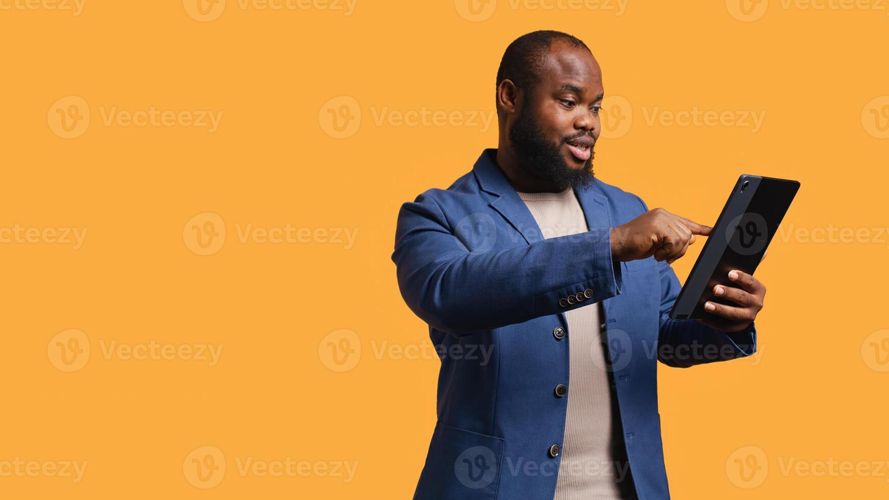 Man happily scrolling on tablet touchscreen to check social media feed. African american person browsing internet websites, entertained by content, studio background, camera B photo