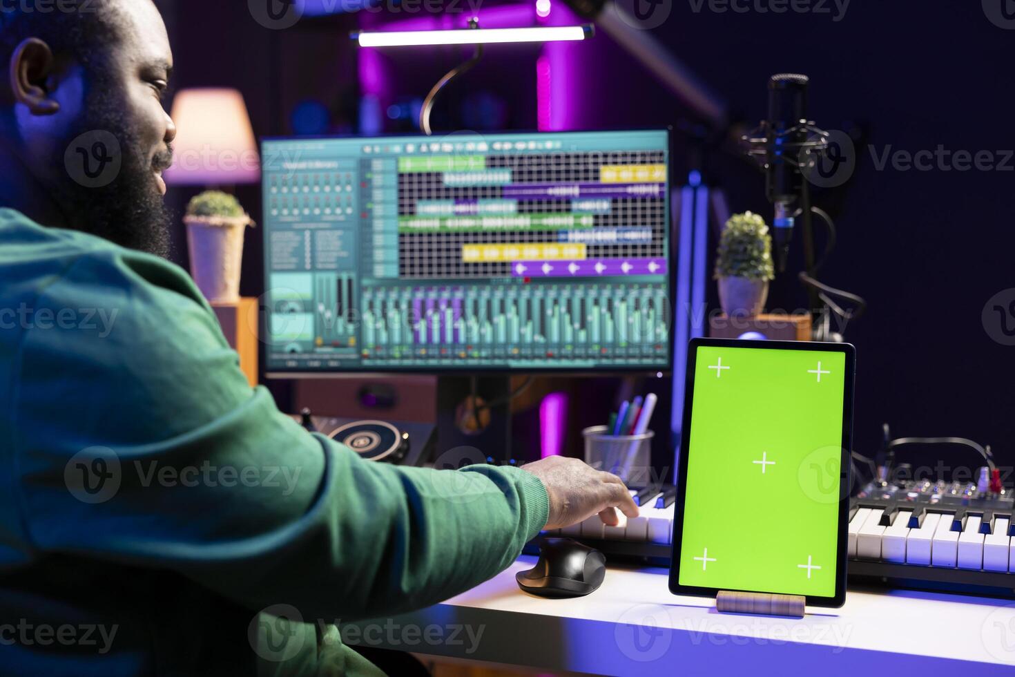 Sound designer producing new soundtracks with digital software, having a tablet with greenscreen on desk. Young talented artist mixing and mastering his audio files, editing in post production. photo