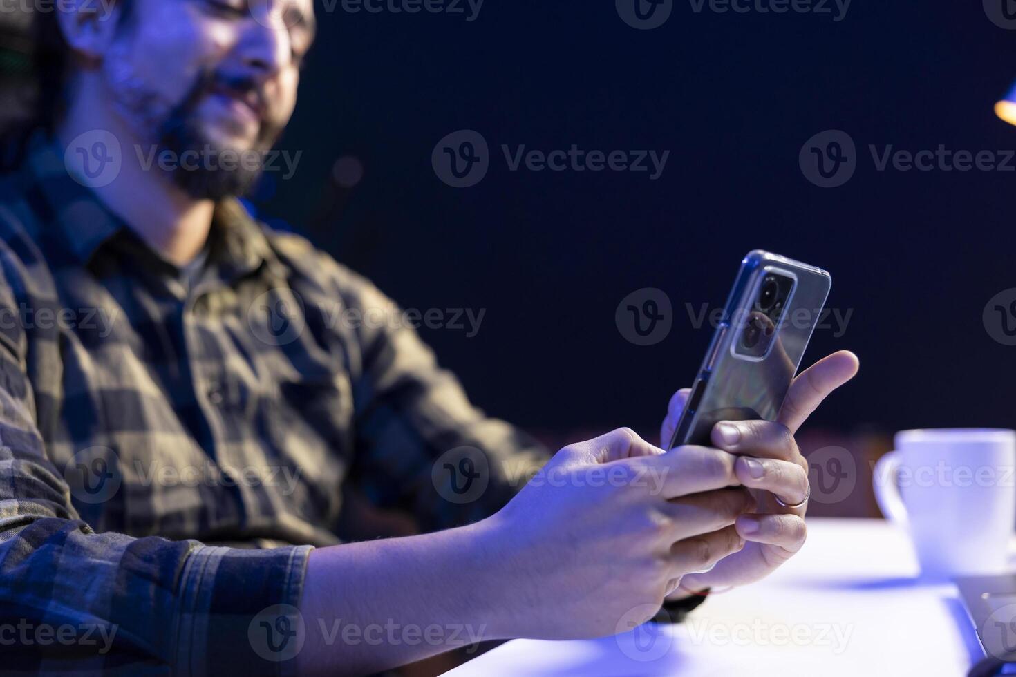 Closeup of young man sitting and using his mobile device for communication, chatting with friends. Male individual grasping his smartphone, browsing the internet, checking social media. photo