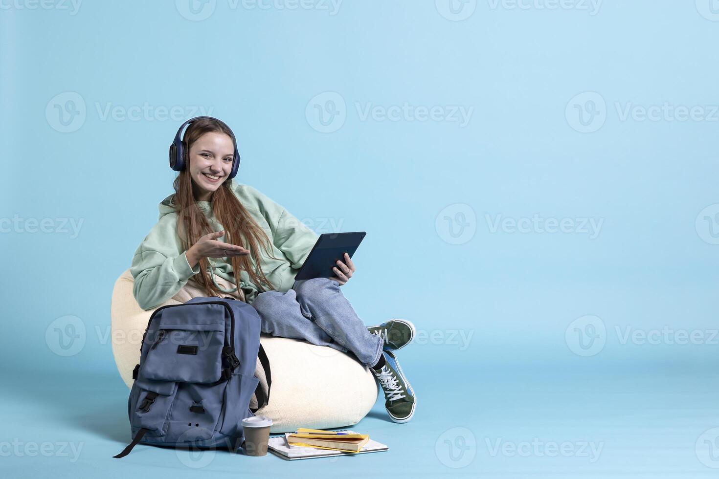 Smiling teenager wearing headphones having fun, using tablet, being entertained. Jolly person relaxing by listening music, picking songs in playlist on device, studio background, photo