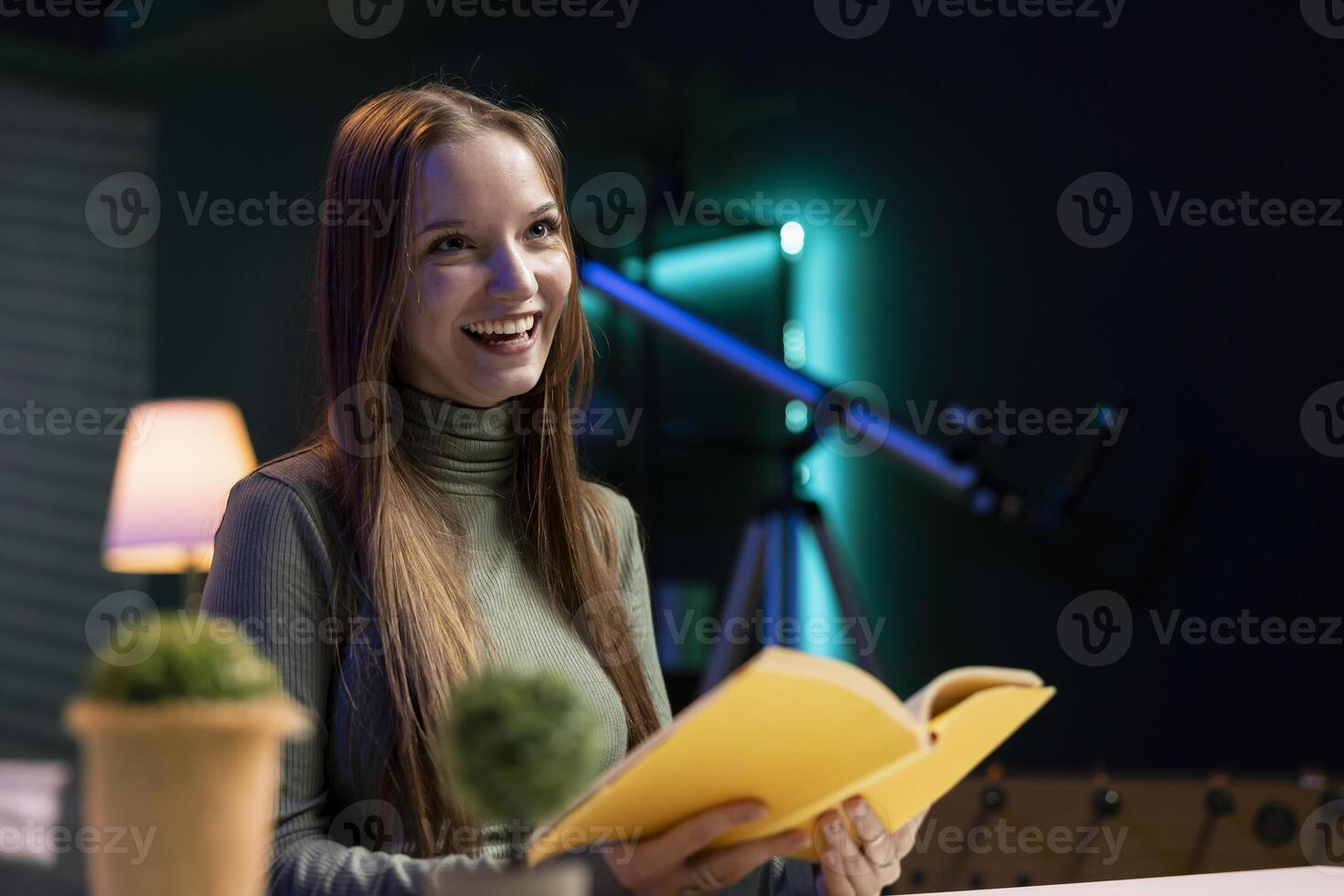Cheerful young content creator films review of book, browsing through pages, presenting synopsis to audience. Happy internet star sponsored by publisher to show new novel release to readers photo