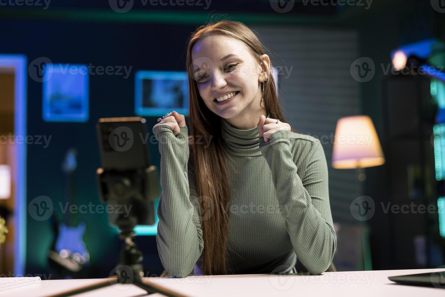 Happy content creator records introductory with smartphone, inviting viewers to subscribe to online channel. Media star uses phone to film herself connecting with watching audience photo