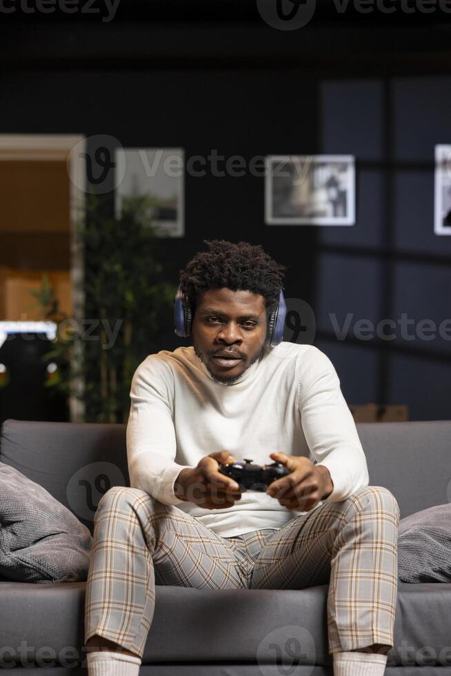 Man playing shooter videogame in stylish apartment, holding joystick. Gamer participating in online esports tournament using professional gamepad and headphones for better victory chances photo