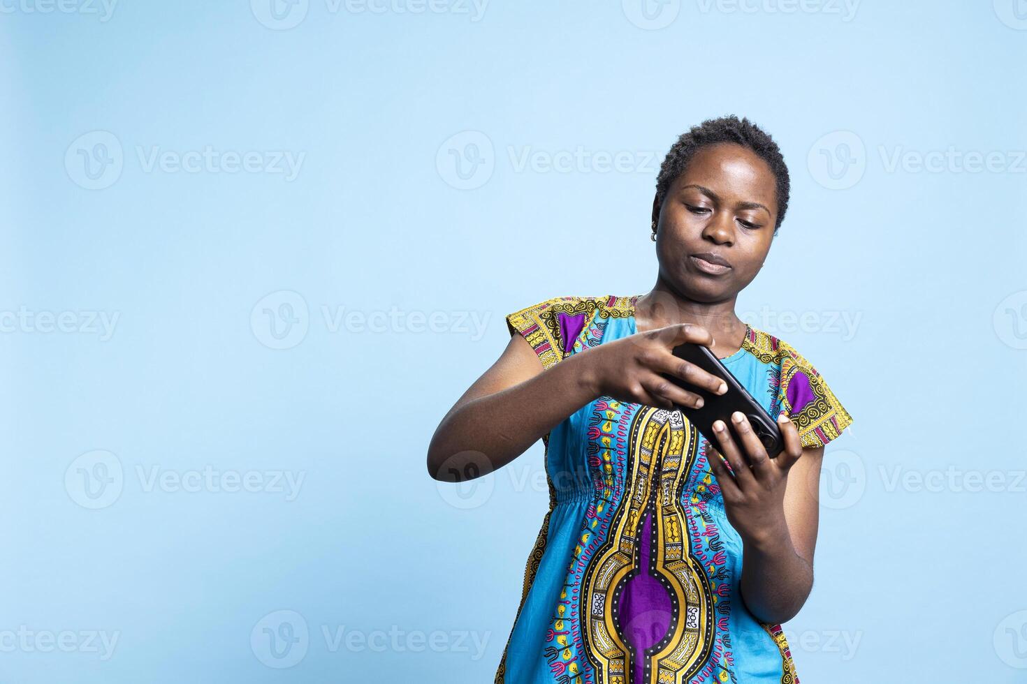 Cheerful woman playing online games on phone app, having fun with e sport tournament over blue background. Young adult enjoys gaming competition with mobile gameplay on camera. photo