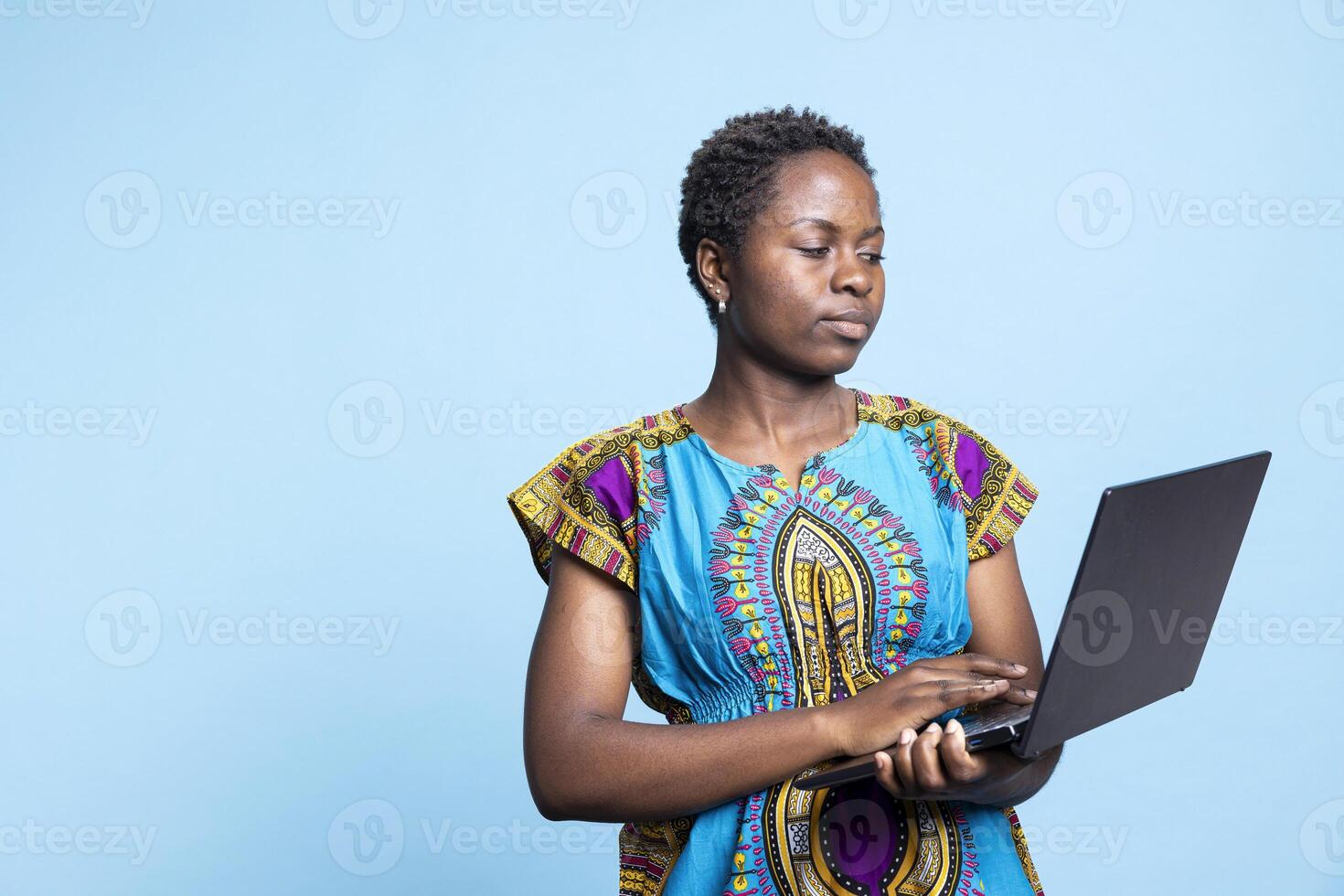 African american woman working on a laptop in front of the camera, using wireless pc to check social media and web pages. Young adult typing information online, internet connection in studio. photo