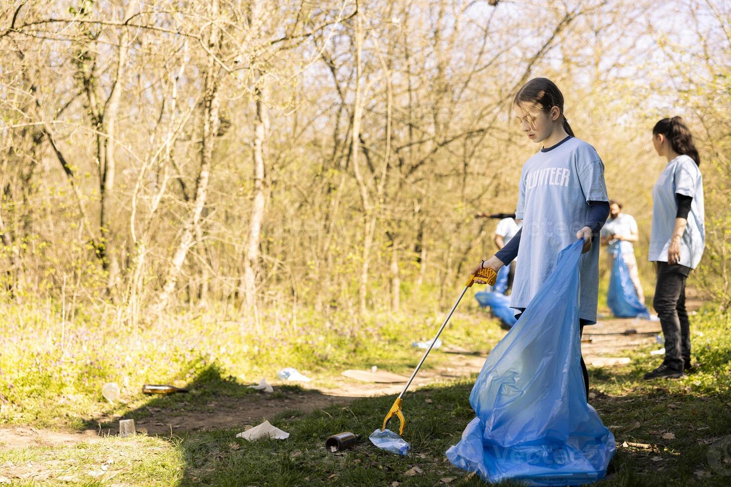 Sweet child volunteer picking up trash and plastic to recycle, working with adults to conserve and restore nature. Little activist combating illegal dumping, collecting rubbish in bags. photo