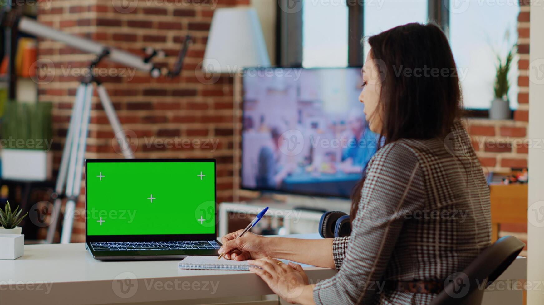 Teleworker staying at home using green screen laptop to do various job tasks at wooden desk. Remote working employee typing data on chroma key notebook keyboard and writing on notepad photo