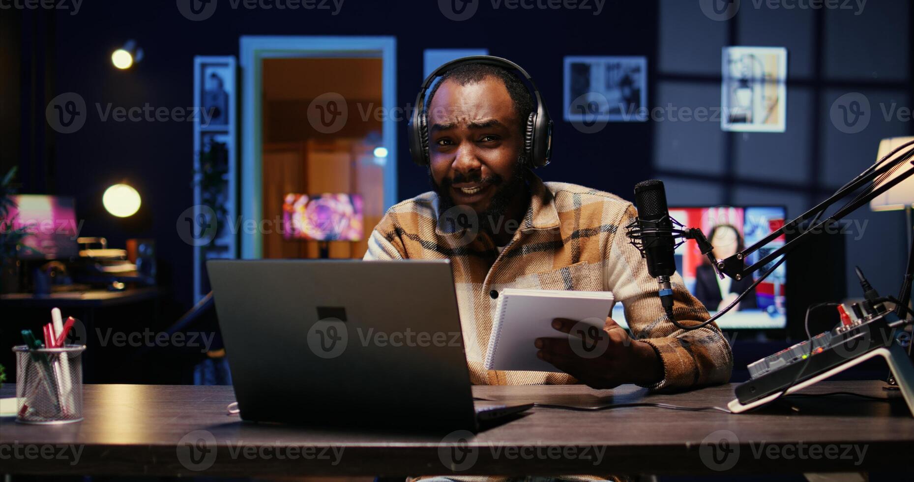 African american media star using outlined ideas on notebook to film vlog channel intro for online streaming platforms. Man following discourse script on paper, presenting today topic photo