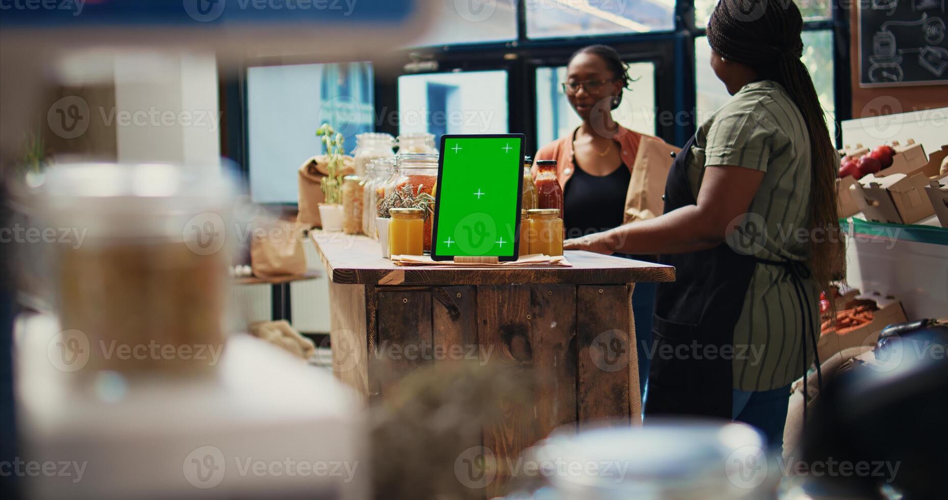 Merchant shows bio products next to greenscreen tablet, working at a local grocery shop and farming. Client checking pasta in jars, gadget running copyspace isolated display layout. Tripod shot. photo