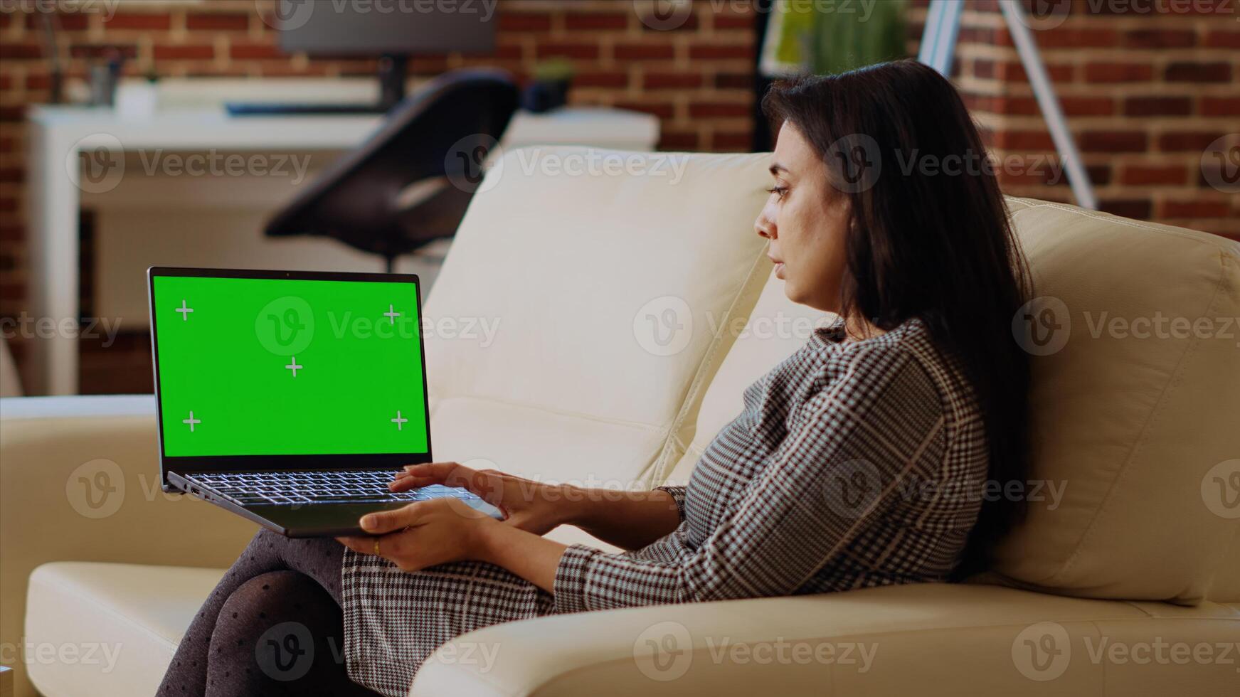 Freelancing businesswoman staying at home using isolated screen laptop to do various job tasks. Remote working indian person typing data on mockup notebook keyboard, sitting on cozy couch photo