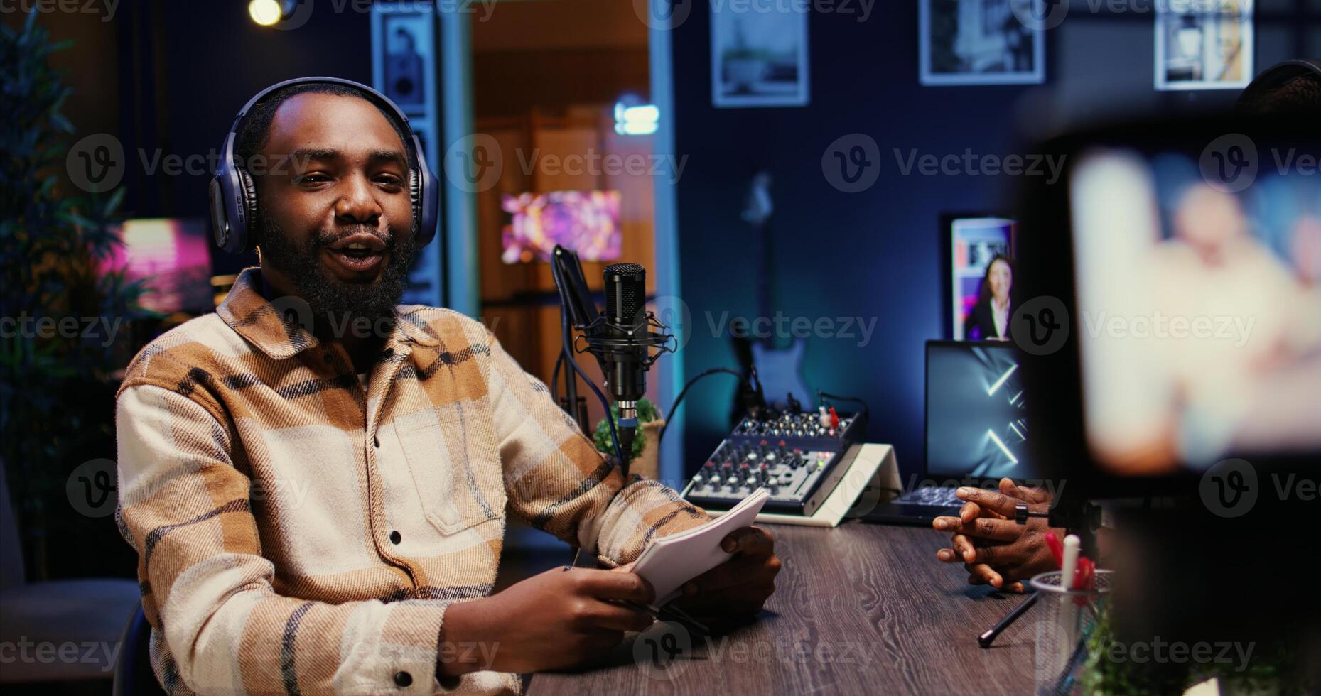 BIPOC man on podcast conversating with guest during marathon stream for charitable cause. Host in apartment studio chatting with celebrity, gathering donations from fans during online show photo