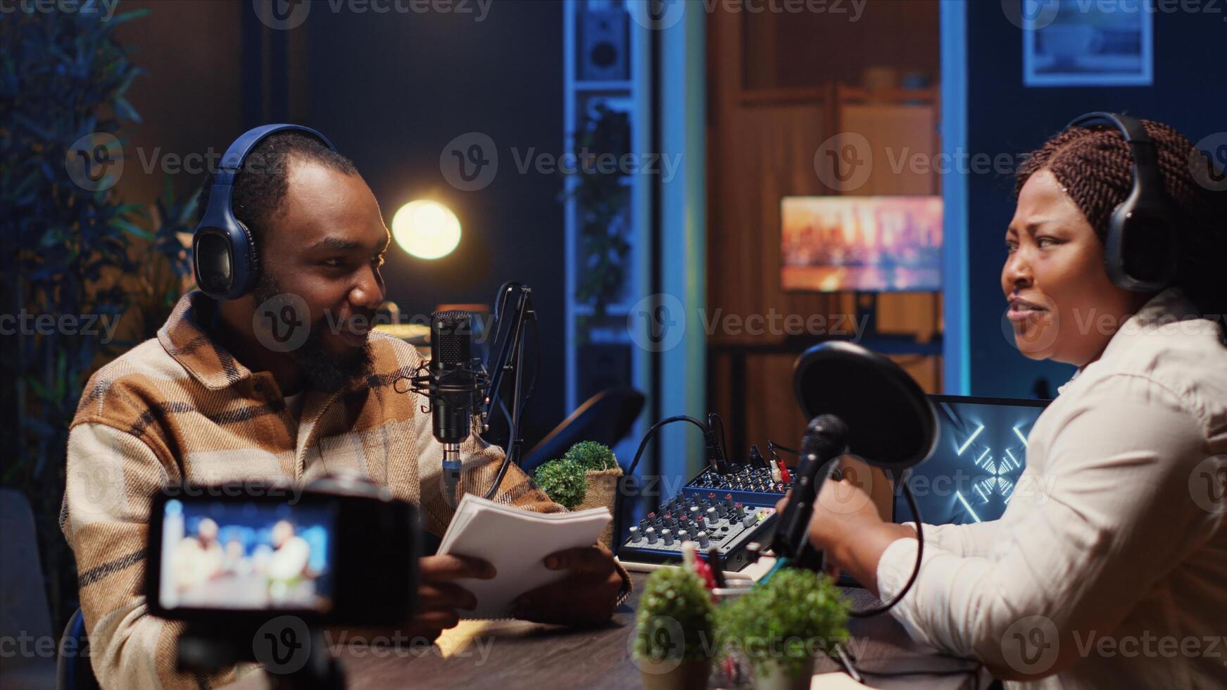 Internet show host making woman laugh, cracking jokes during comedy focused podcast filmed with professional gear. Talking show interviewer broadcasting live from studio with recording camera photo