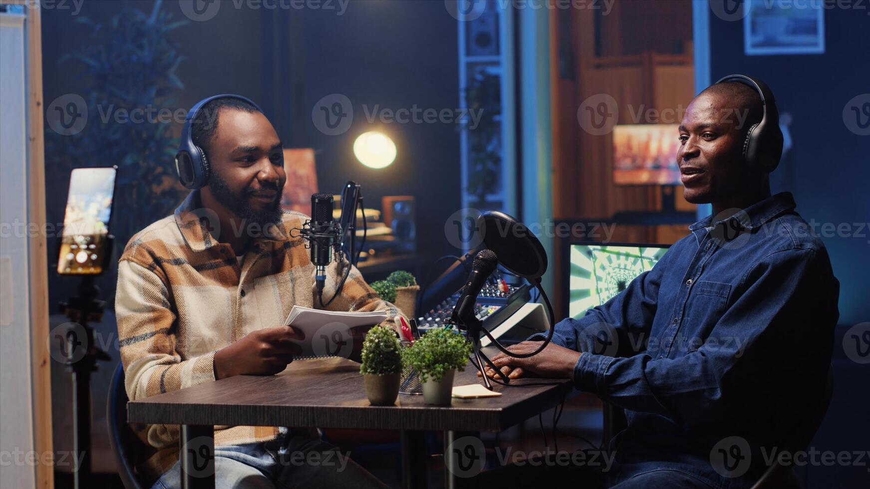 Man recording podcast using smartphone attached to tripod and high tech microphones to interview guest, ensuring flawless and sound quality for audience watching at home photo