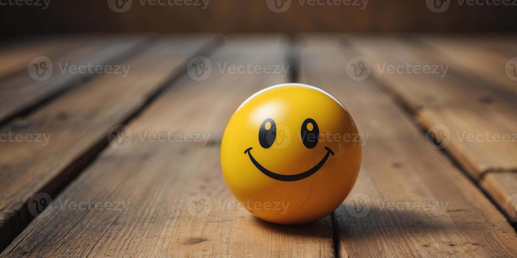 A yellow ball with a smiley face drawn on it sits on a wooden floor. photo