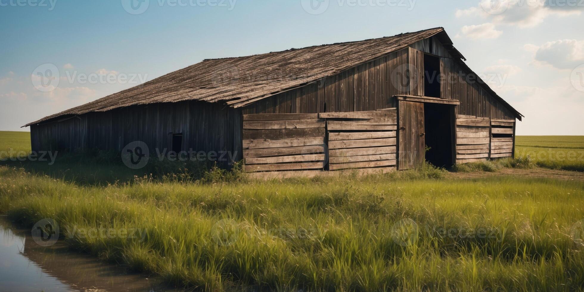 Weathered barn with a deteriorating roof in a green field near a blue water ditch on a sunny spring day. photo