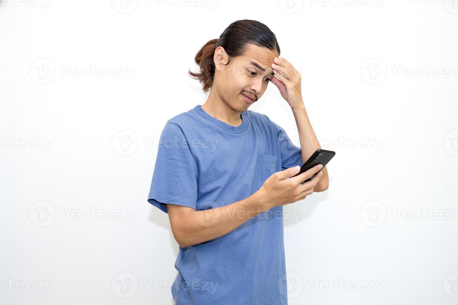An Asian young man wearing a dark blue shirt is dizzy, and holding a cellphone. With a thoughtful expression. photo