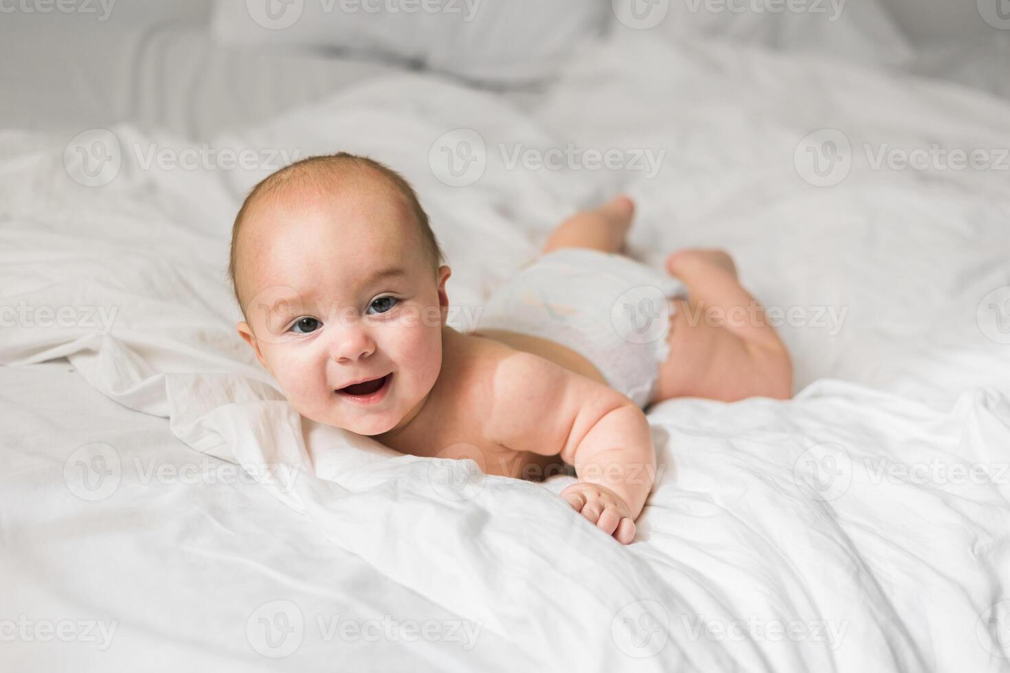 Smiling newborn baby on a white bed at home, the concept of a happy healthy infant baby. Generation alpha and gen alpha photo