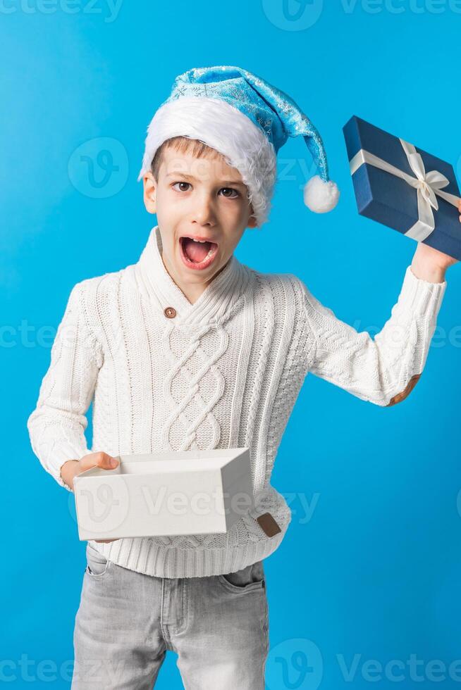 Surprised Child boy gift. Kid in blue christmas hat holds gift box. Shopping time, copy space and empty space for text. Generation alpha and gen alpha photo