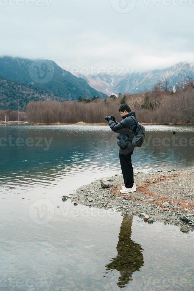 man tourist travel Kamikochi National Park, happy Traveler sightseeing Taisho pond with mountain, Nagano Prefecture, Japan. Landmark for tourists attraction. Japan Travel, Destination and Vacation photo