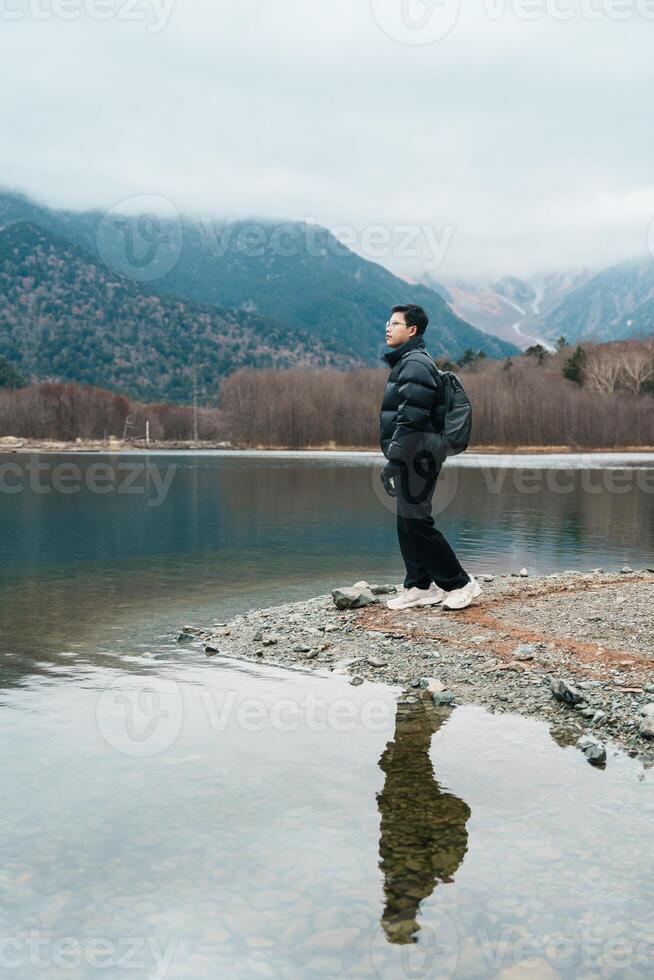 man tourist travel Kamikochi National Park, happy Traveler sightseeing Taisho pond with mountain, Nagano Prefecture, Japan. Landmark for tourists attraction. Japan Travel, Destination and Vacation photo