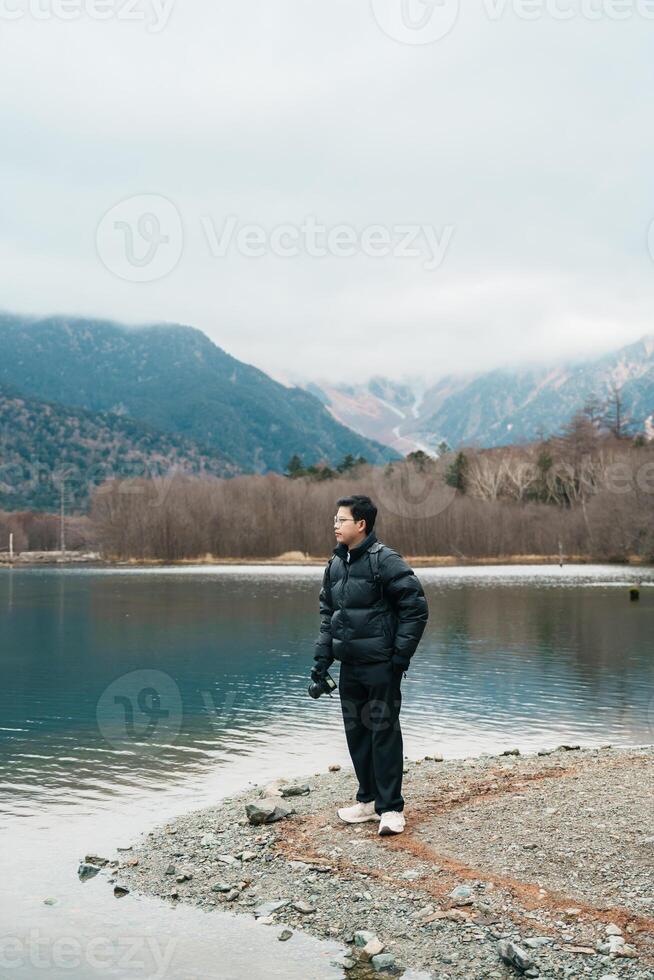 man tourist travel Kamikochi National Park, happy Traveler sightseeing Taisho pond with mountain, Nagano Prefecture, Japan. Landmark for tourists attraction. Japan Travel, Destination and Vacation photo