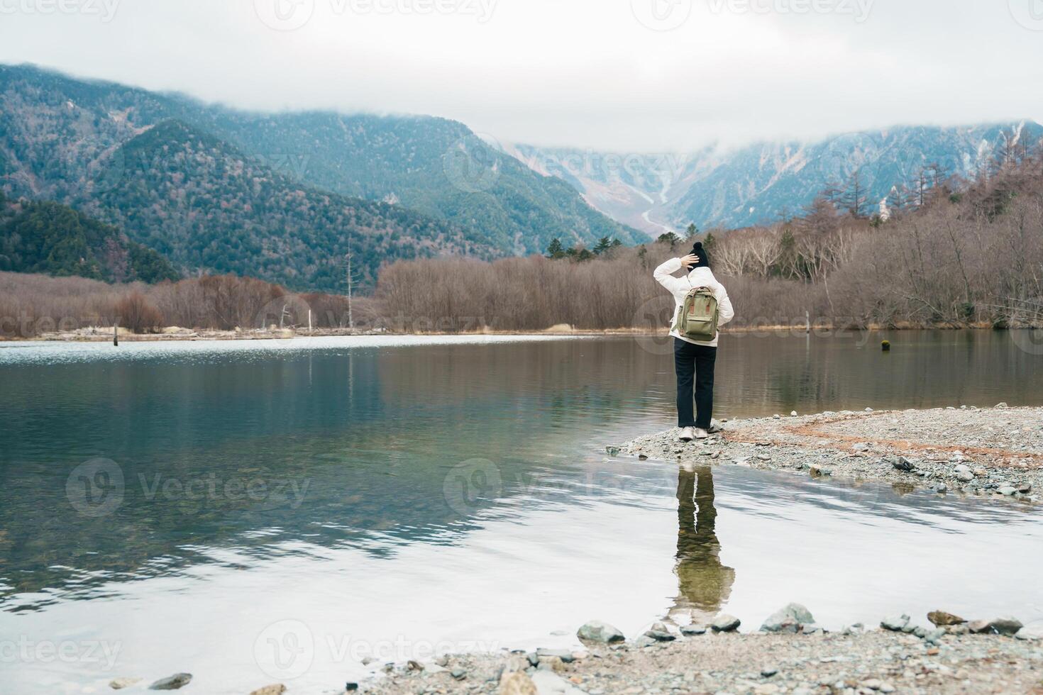 Woman tourist travel Kamikochi National Park, happy Traveler sightseeing Taisho pond with mountain, Nagano Prefecture, Japan. Landmark for tourists attraction. Japan Travel, Destination and Vacation photo