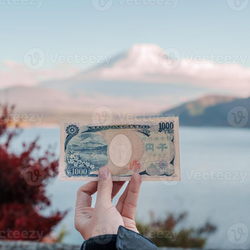 Hand holding 1000 yen banknote with mount Fuji at Lake Motosu, happy tourist travel Mt Fuji and road trip Fuji Five Lakes. Landmark for tourists attraction. Japan Travel, Destination and Vacation photo