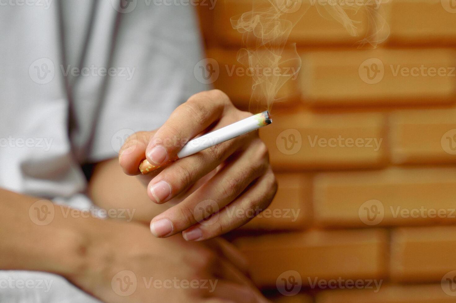 Asian man's hand holds a lit cigarette and sits alone smoking in the smoking corner of his house. photo