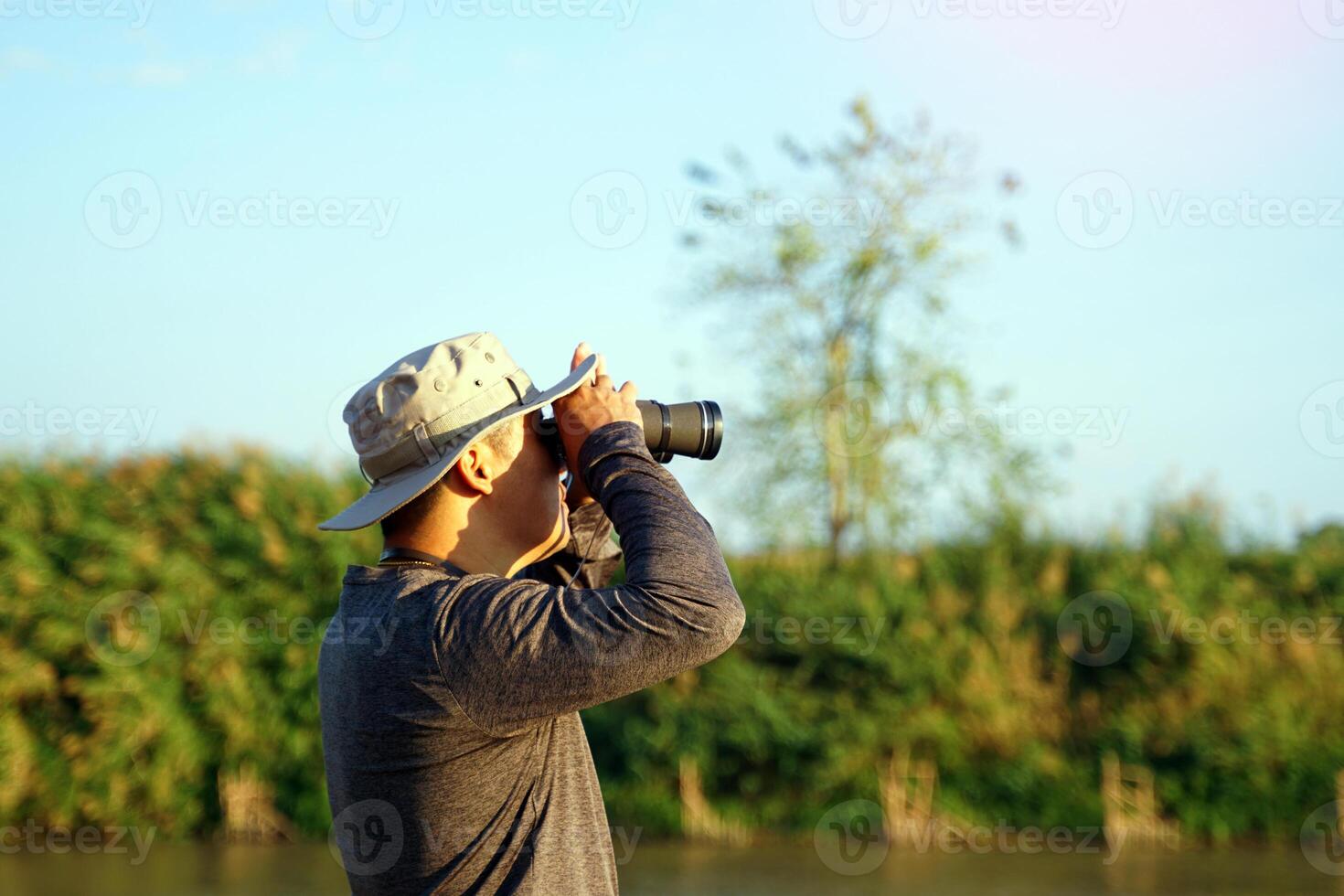Asian man uses binoculars to observe local birds along a river. Soft and selective focus photo