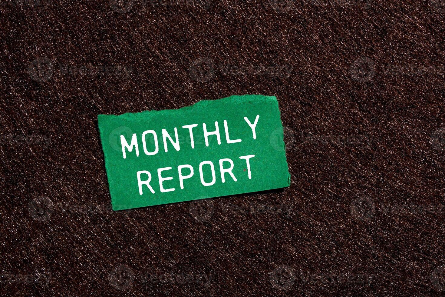 Monthly report message written on ripped torn green paper piece on brown background. Conceptual monthly report symbol. Copy space. photo