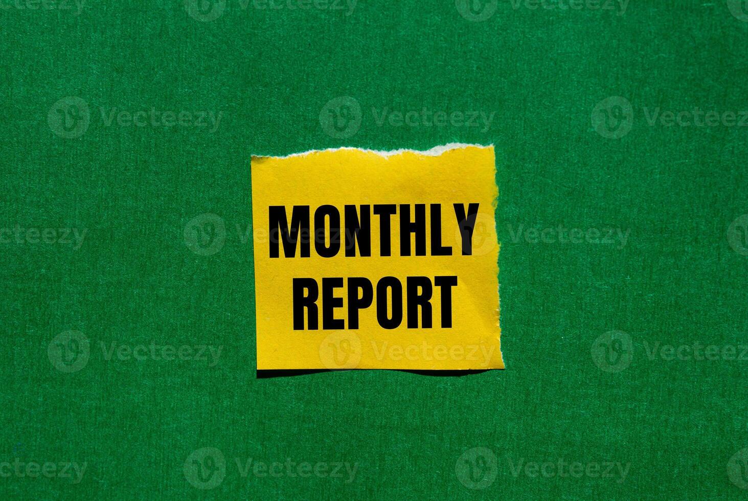 Monthly report message written on ripped torn yellow paper piece on green background. Conceptual monthly report symbol. Copy space. photo
