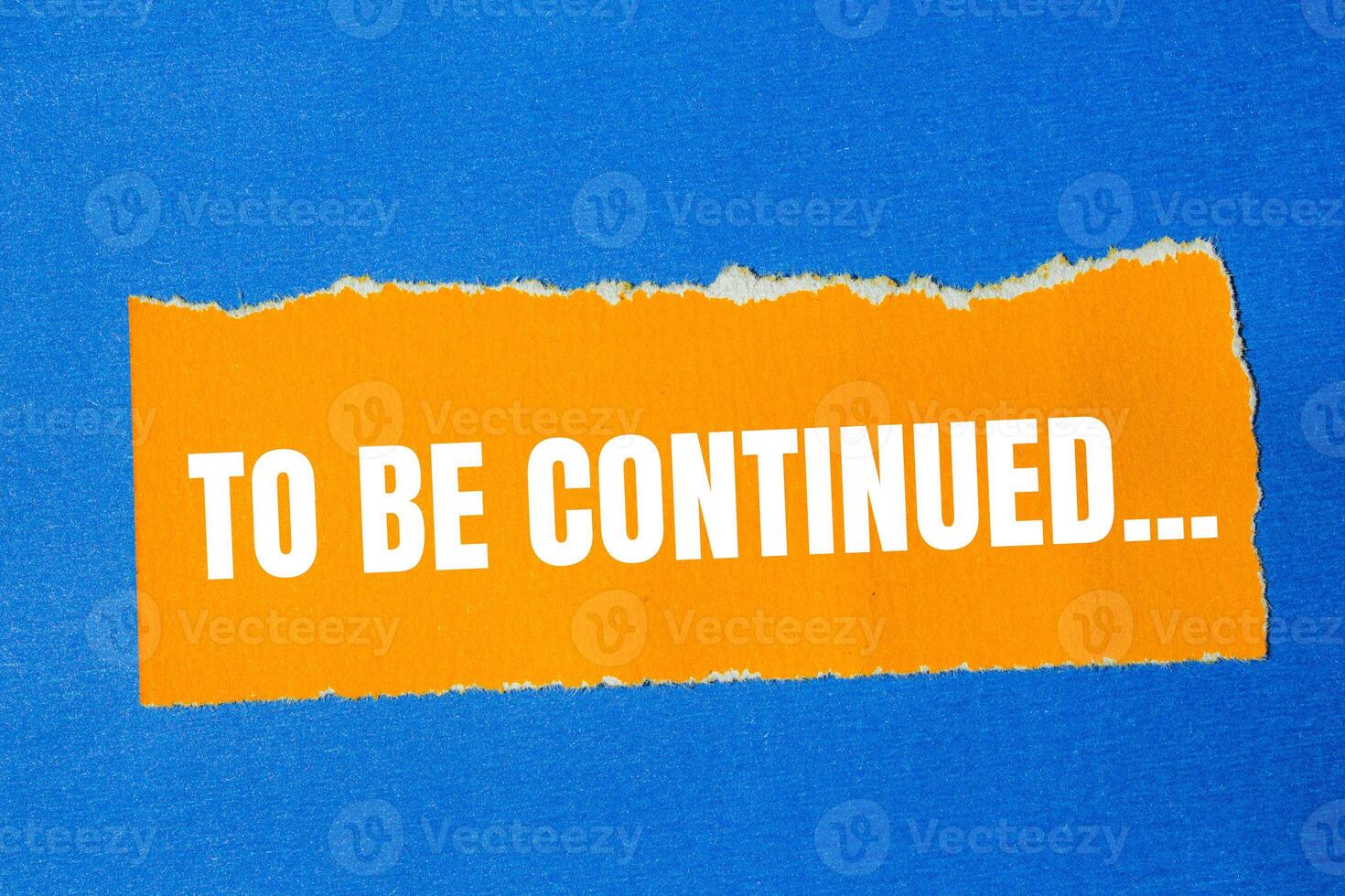 To be continued message written on ripped torn orange paper with blue background. Conceptual to be continued symbol. Copy space. photo