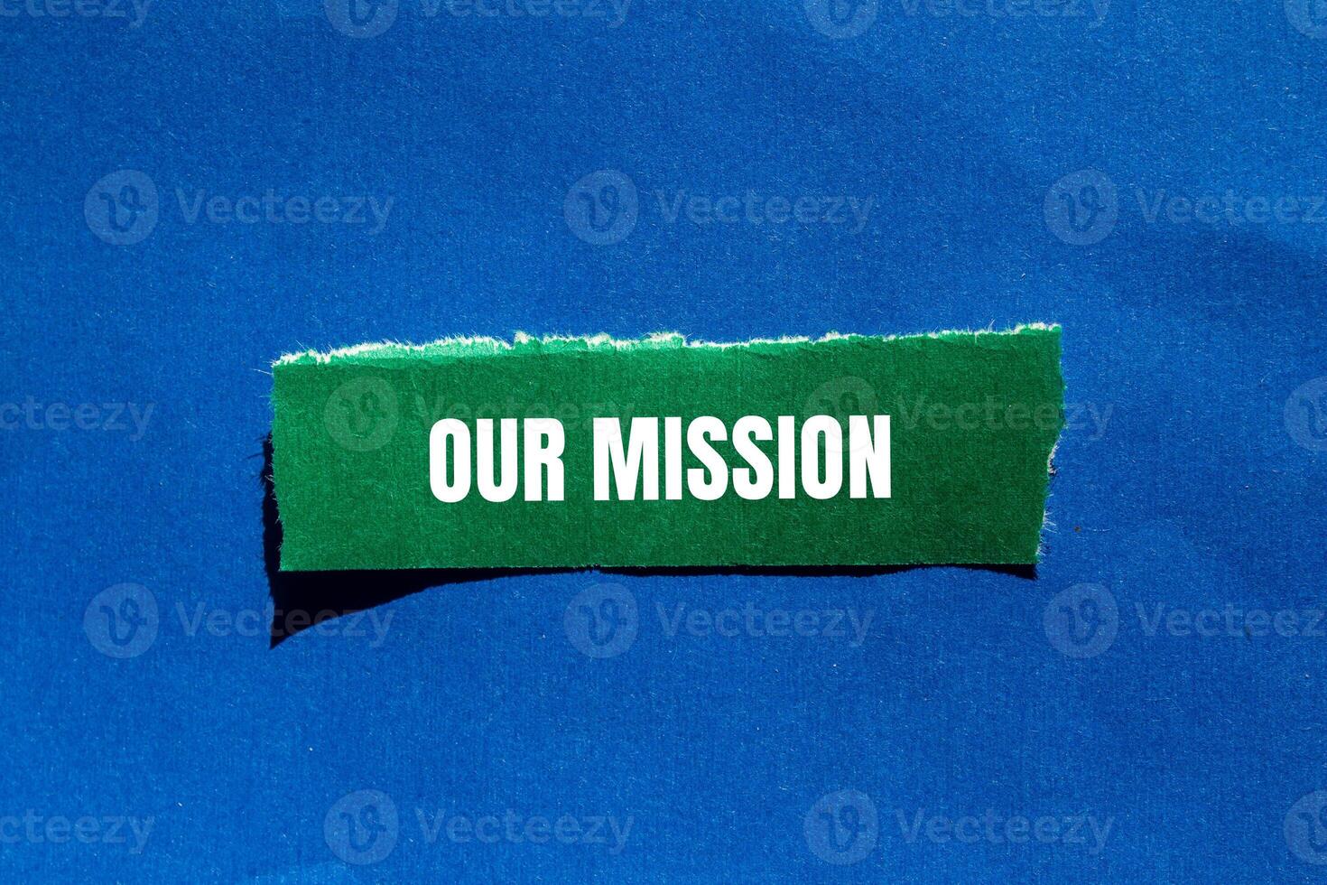 Our mission message written on ripped torn green paper piece on blue background. Conceptual our mission symbol. Copy space. photo