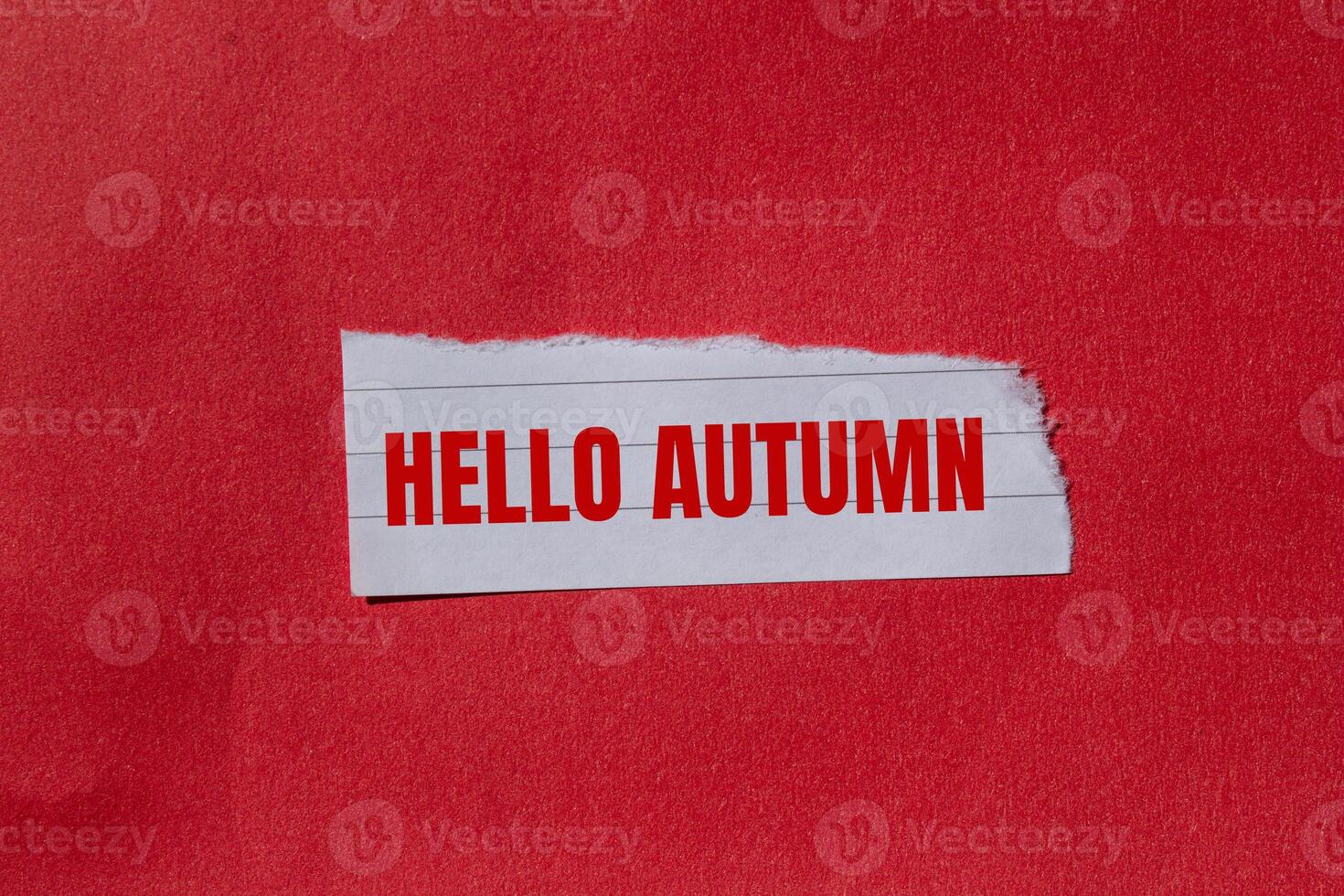 Hello autumn message written on ripped torn paper piece with red background. Conceptual hello autumn symbol. Copy space. photo